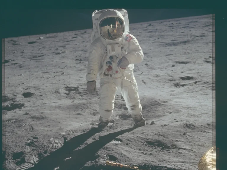 Buzz Aldrin sobre la superficie lunar durante Apolo 11, con huellas en el suelo y el reflejo de Neil Armstrong en su visor.