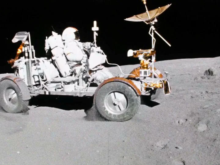 John Young conduciendo el vehículo lunar del Apolo 16 mientras las ruedas levantan polvo sobre la superficie de la Luna.