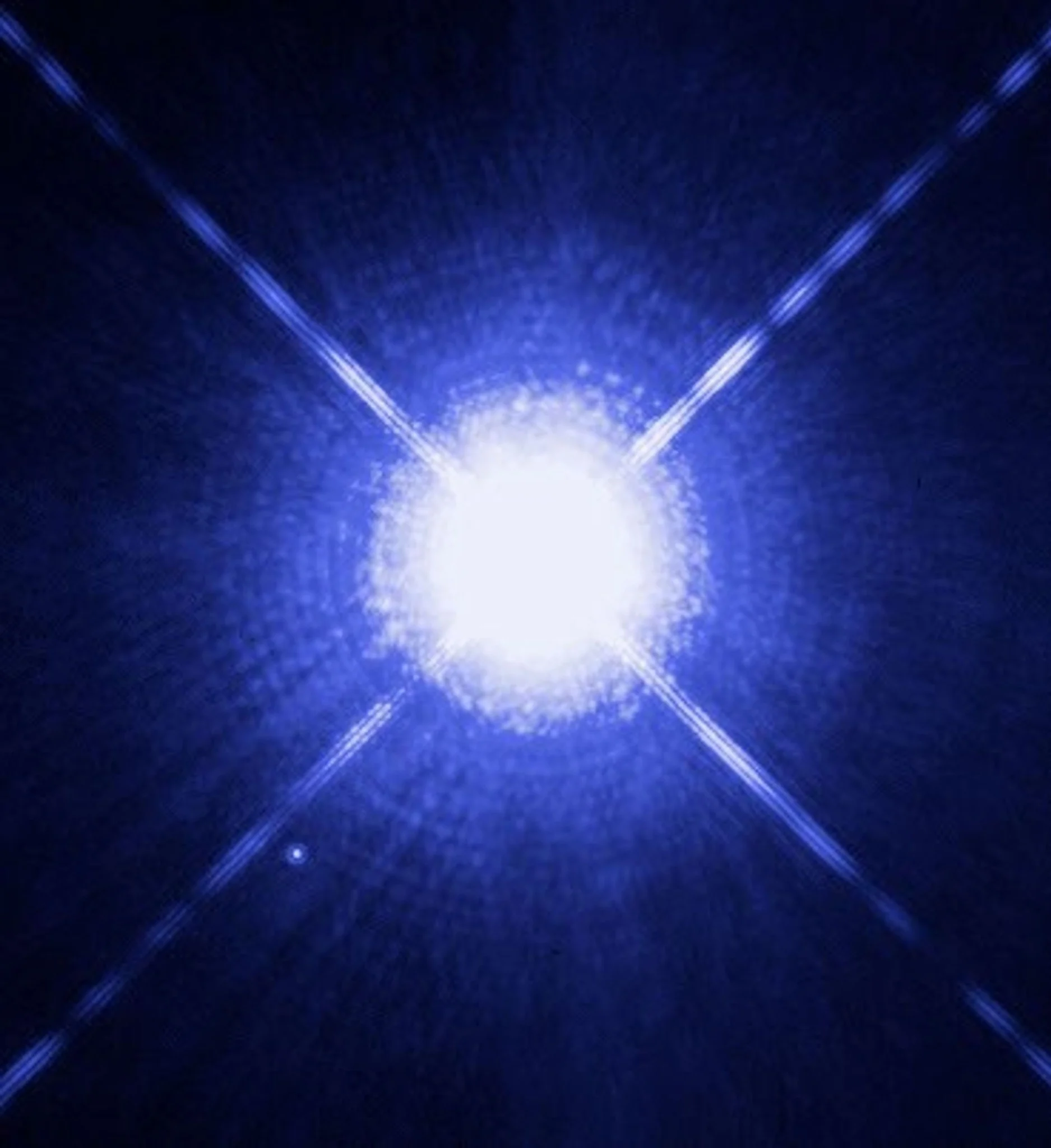 Fotografía del sistema estelar Sirio tomada por el telescopio espacial Hubble, con Sirio A sobreexpuesta en el centro y Sirio B visible como un pequeño punto luminoso abajo a la izquierda.